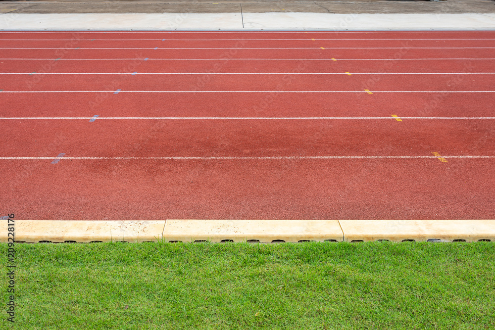 Fototapeta premium White lines of stadium and texture of running racetrack red rubber racetracks in outdoor stadium are 8 track and green grass field,empty athletics stadium with track.