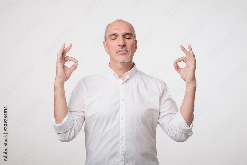 Concentrated mature man in white shirt tries to relax after hard working day, daydreams, keeps fingers together. Meditation and relax concept. Concentrated mature man in white shirt tries to relax after hard working day, daydreams, keeps fingers together. Meditation and relax concept.