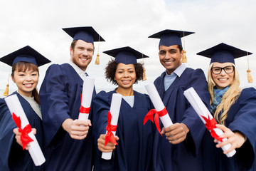 education, graduation and people concept - group of happy international students in mortar boards and bachelor gowns with diplomas
