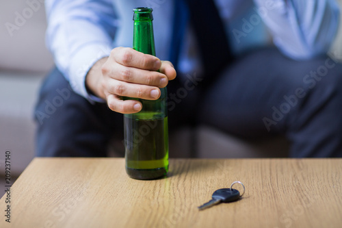 alcohol abuse, drunk driving and people concept - close up of male driver hand with beer bottle and car key on table