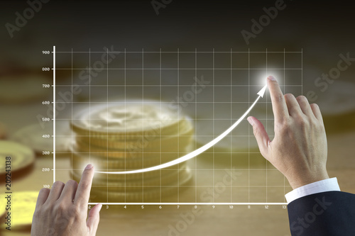 Businessman’s hands drawing a line graph showing of business growth and success with golden tone of money stack on background.