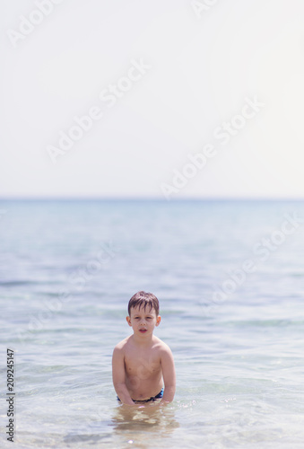 Adorable boy standing in the water on the beach. Family vacation or holiday concept.