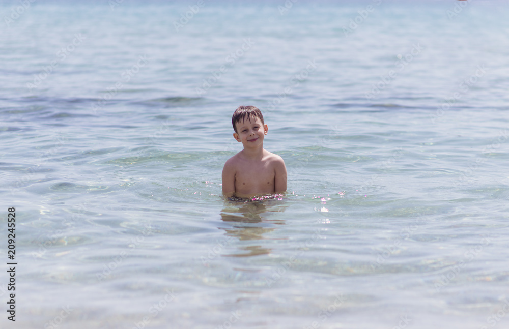 Adorable boy standing in the water on the beach. Family vacation or holiday concept.