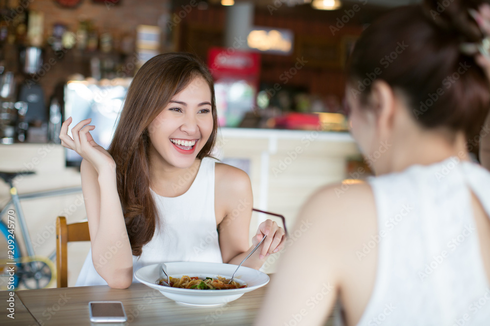 Two young Asia woman friends enjoying food together in a restaurant laughing and joke
