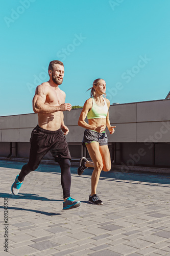 Pretty sporty woman and man jogging at city