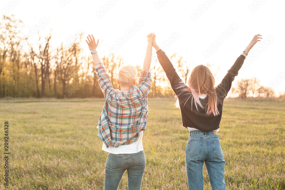 Two young women standing on the field at sunset and rise up hands Two young women standing on the field at sunset and rise up hands