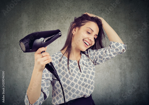 Smiling woman drying her hair with a hairdryer