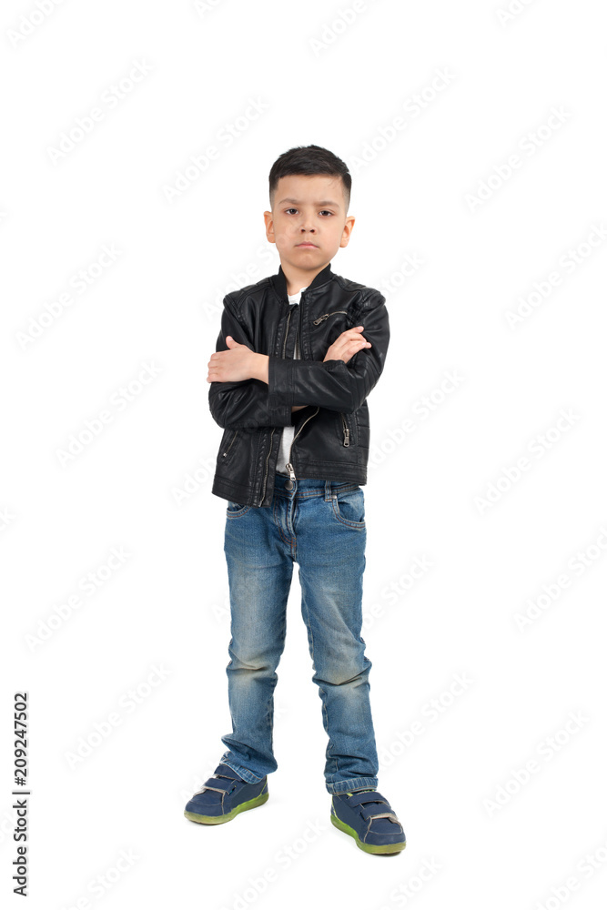 Naklejka premium Full length portrait of the serious little difficult child of the brunette with arms crossed wearing black leather jacket and jeans on a white background in studio.