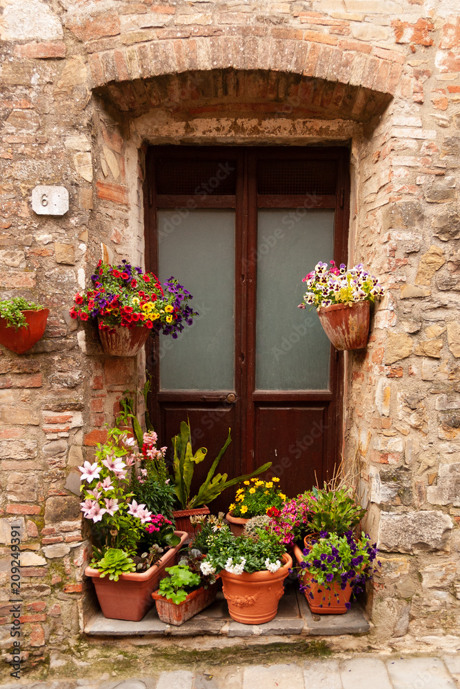 Wooden door surrounded by colorful flowers in Tuscany, Italy.
