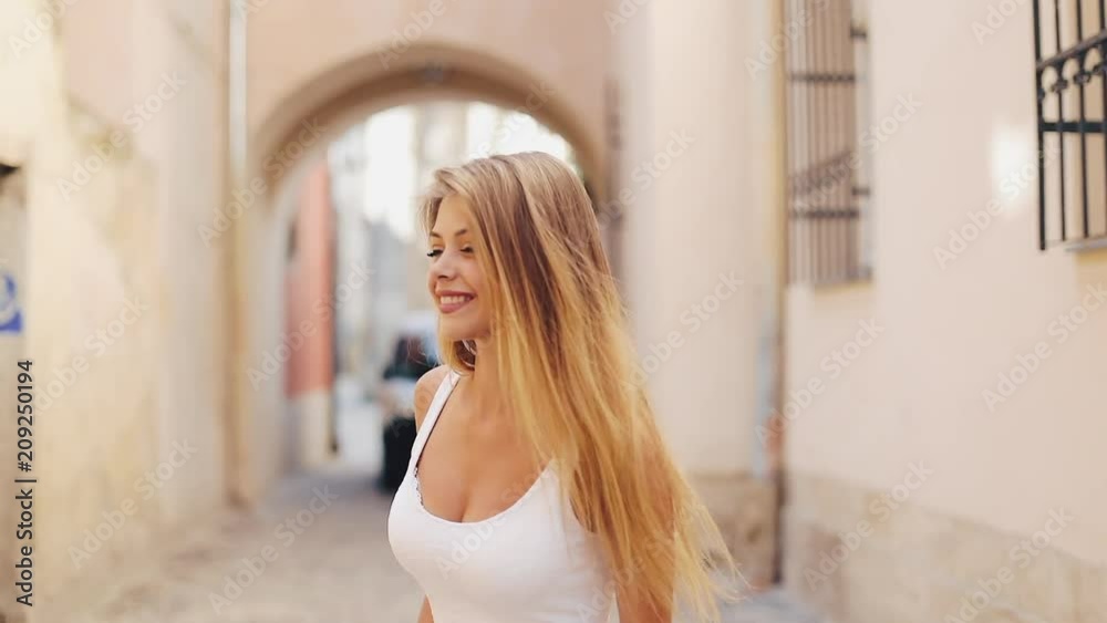 Charming young woman with a in a beautiful white dress with loose hair. Attractive young lady is rushing in the city-center, she turns to camera and smiles. Slow motion Charming young woman with a in a beautiful white dress with loose hair. Attractive young lady is rushing in the city-center, she turns to camera and smiles. Slow motion