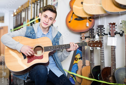 Smiling teenage customer deciding on acoustic guitar