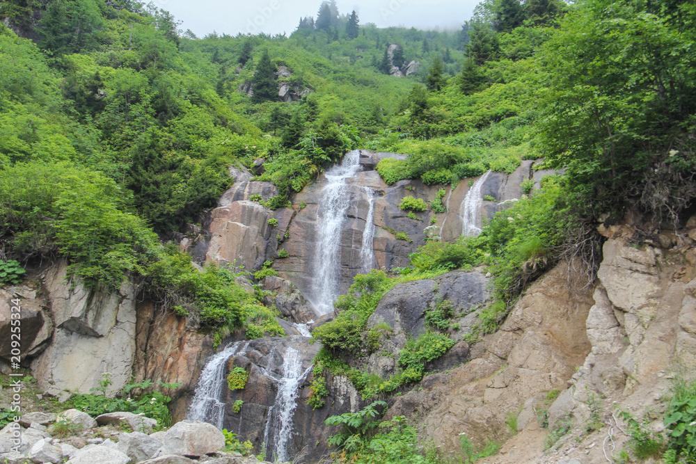Waterfall in mountain forest with silky foaming water and wet stones