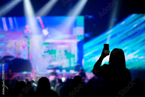 People holding Smartphone take photo crowd in night event hall.Audience and fans club using mobile phone,enjoying and dance in Live concert.Technology concept