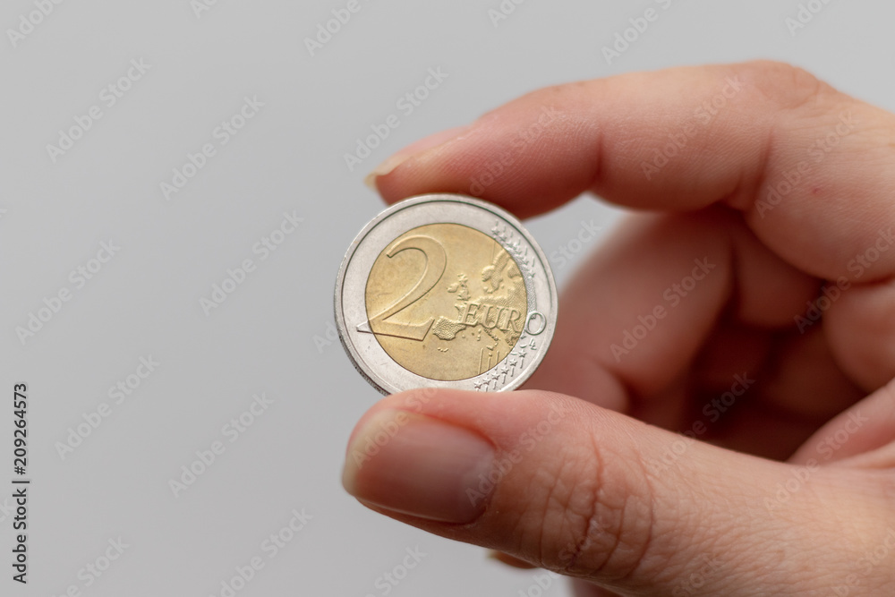 Two Euro coin between the fingers of a woman Two Euro coin between the fingers of a woman