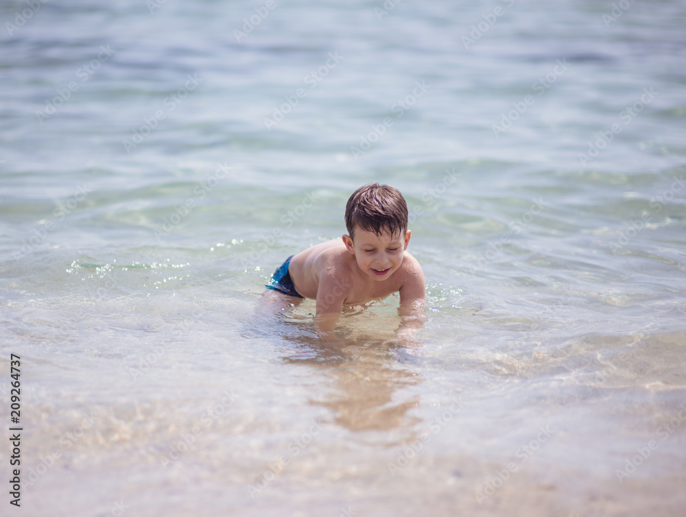 Adorable young kid sitting in the water on the beach