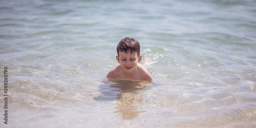 Adorable young kid sitting in the water on the beach