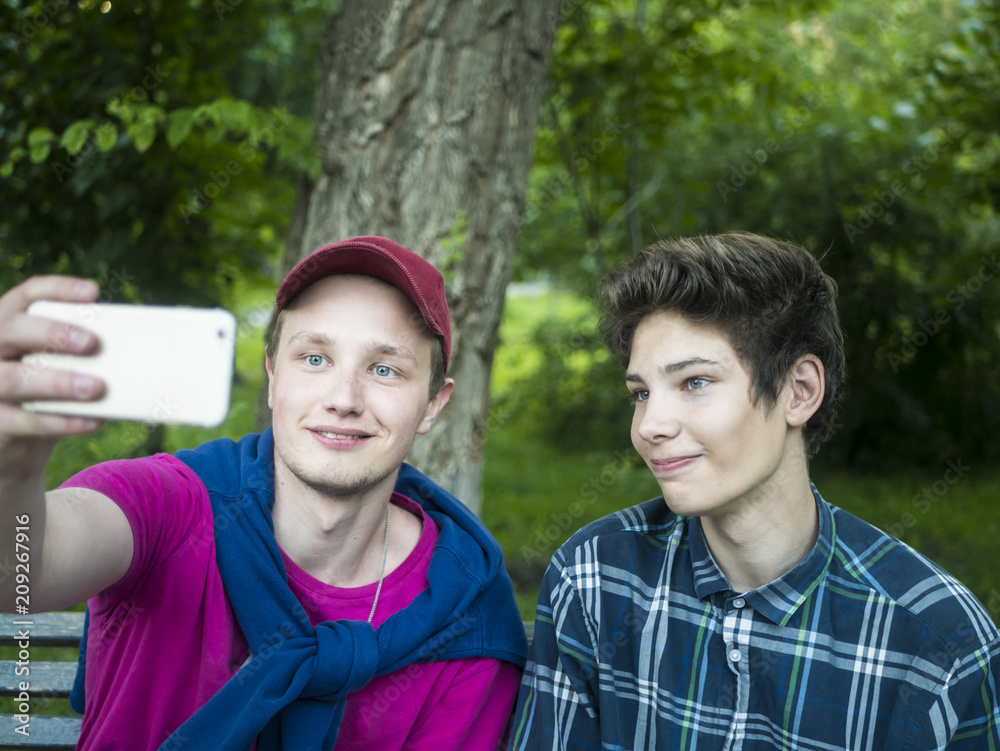 portrait of two young smiling handsome brothers outdoors doing a selfie with phone in the park portrait of two young smiling handsome brothers outdoors doing a selfie with phone in the park