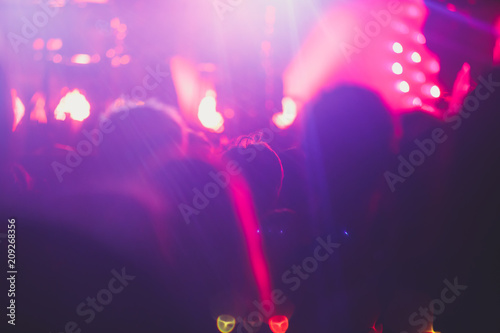 A crowded concert hall with scene stage lights, rock show performance, with people silhouette and hand holding smartphone