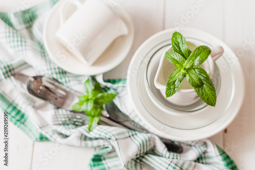 Clean glass and ceramic dishes with mint sprigs on a white wooden table. Preparing for breakfast. Soft focus.