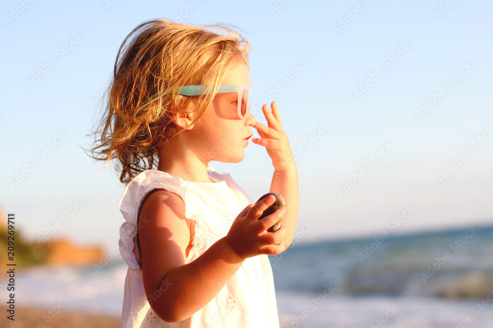 A little cute baby girl is playing on a beach near a sea. Family, summer vacation concept.