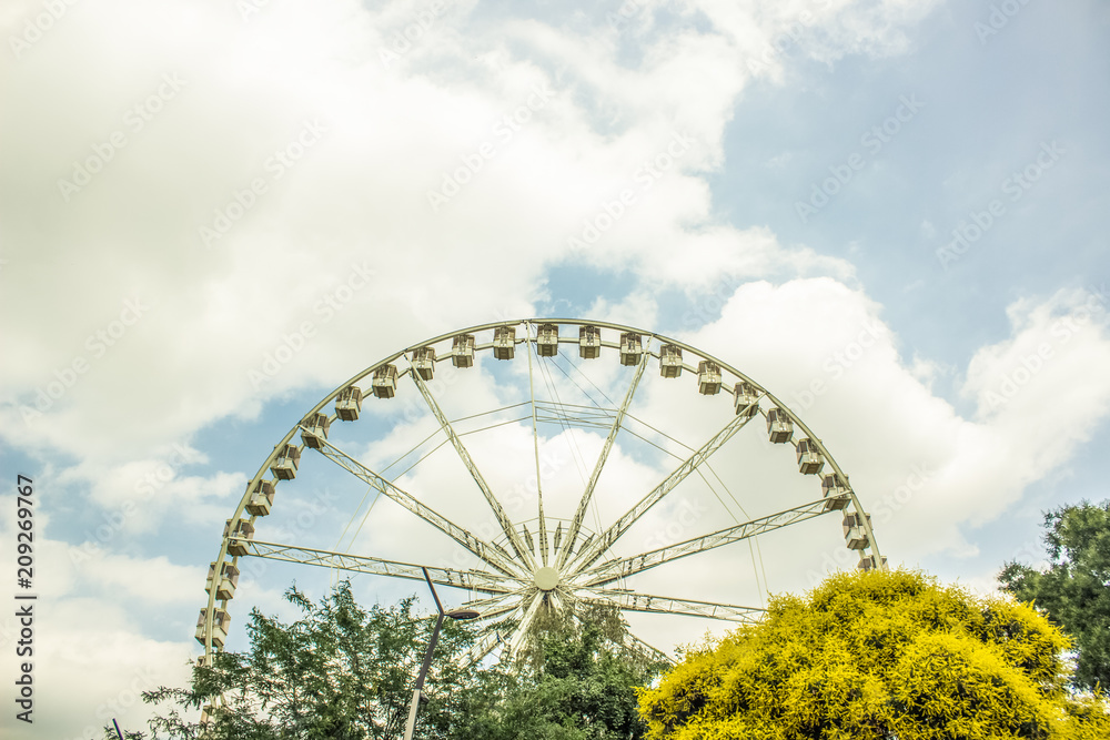 Fototapeta premium ferris wheel above trees and blue cloudy sky