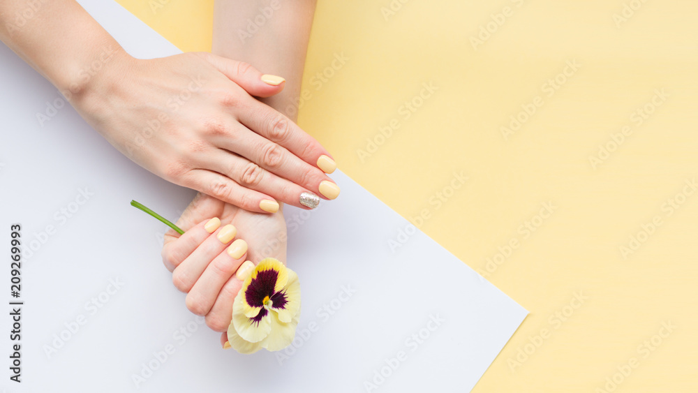 Obraz premium Stylish trendy female manicure. Beautiful young woman's hands on yellow and white background.