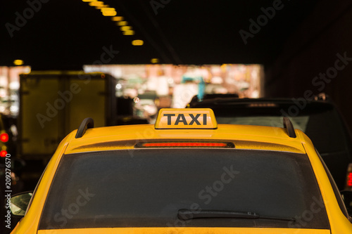 Yellow taxi moves in the midst of cars along city streets.