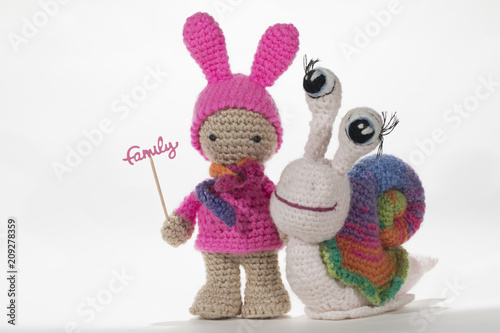 Crochet girl holding sign FAMILY and crochet rainbow snail, on white background. Amigurumi. Handmade