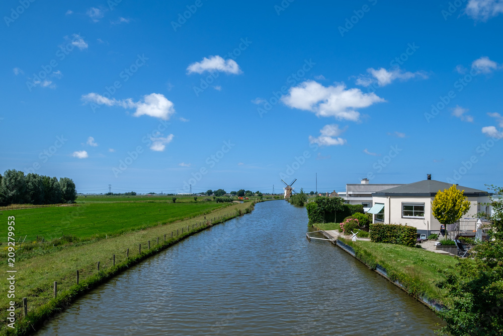 Typical Dutch polder with polder canal and polder mill at the horizon. This historical windmill is from 1719. Province South-Holland, the Netherlands Typical Dutch polder with polder canal and polder mill at the horizon. This historical windmill is from 1719. Province South-Holland, the Netherlands