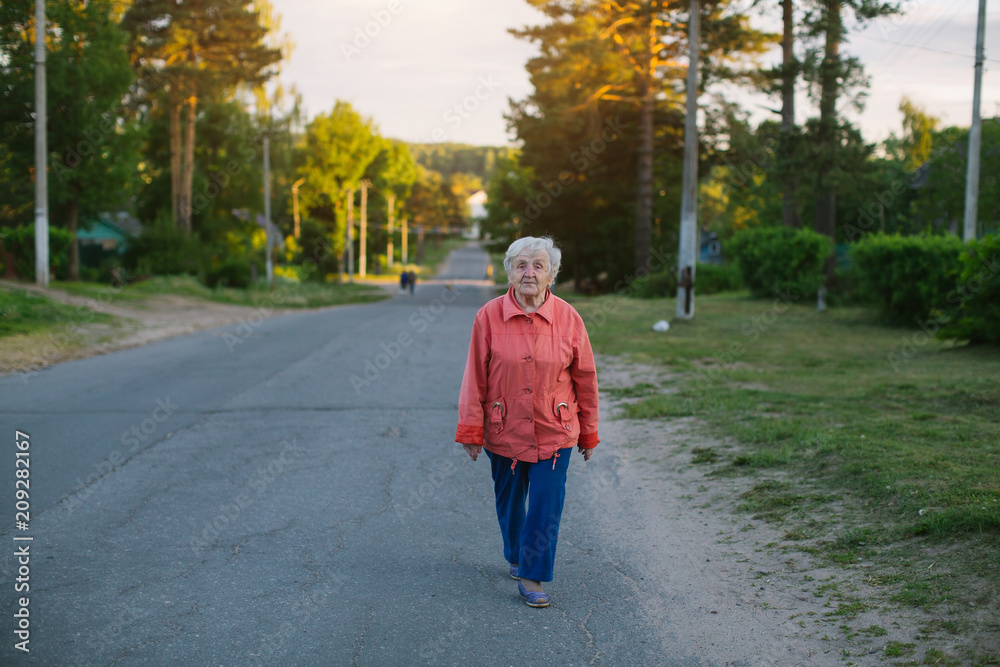 An elderly woman is walking down the street in the village. An elderly woman is walking down the street in the village.