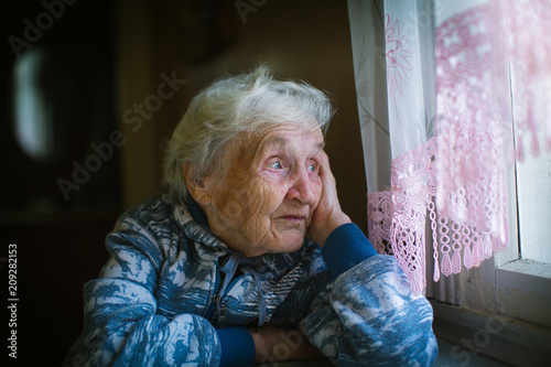 An elderly pensioner woman looks out the window sadly.