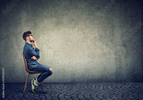 Pensive man sitting against gray photo