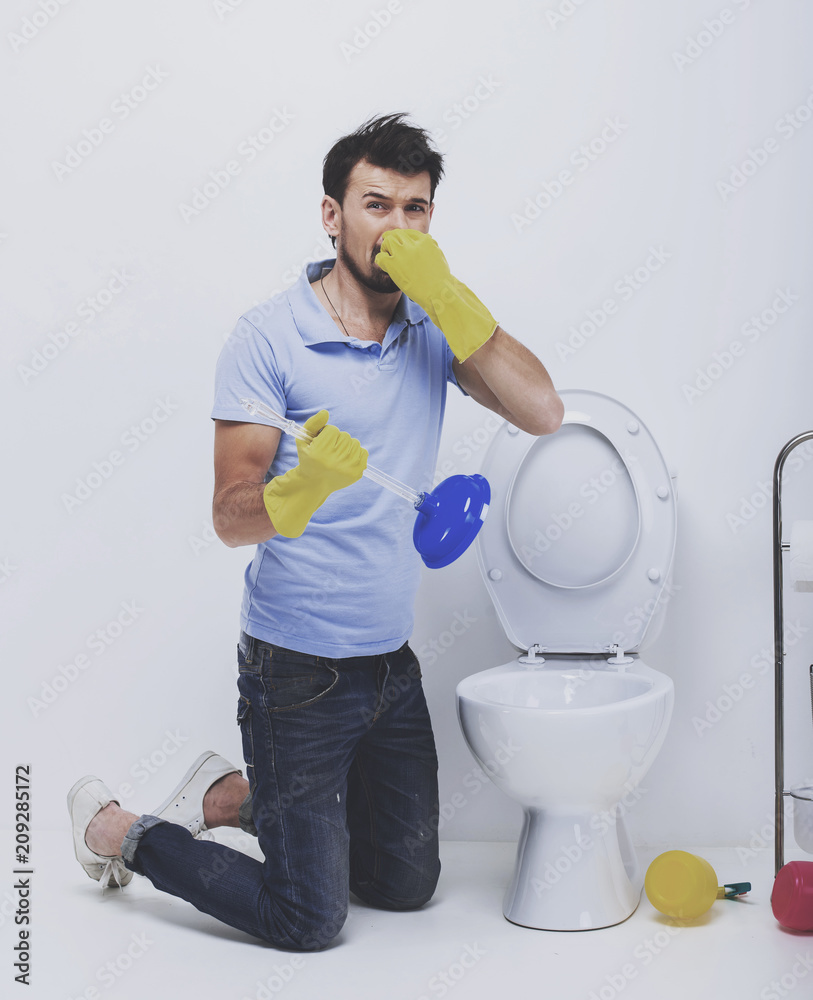 Young man covering nose to avoid bad smell while cleaning smelly toilet bowl.