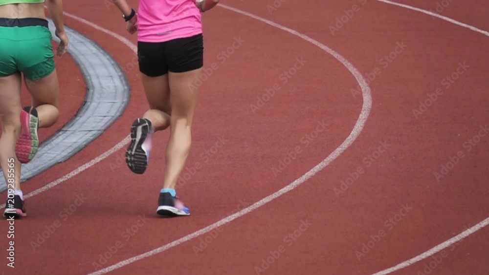 Two slim sporty girls in shorts running around the stadium in slow motion. Rear view Two slim sporty girls in shorts running around the stadium in slow motion. Rear view