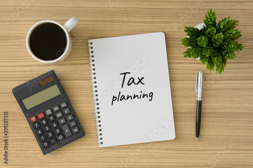 Tax planning written on notebook. Top view of wood desk with office supply.