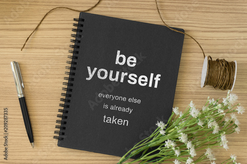 Notebook with motivational and inspirational wisdom quote on wood desk. Be yourself, everyone else is already taken.