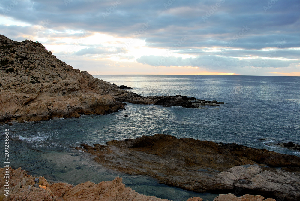 ocean and tide pool on rocky coastline with gray clouds above orange horizon