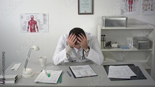 Doctor tired and holding his head at medical cabinet