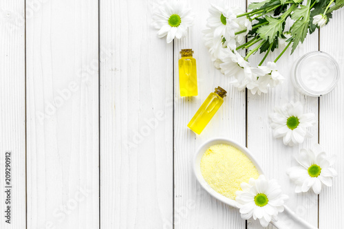 Cosmetics for skin care with chamomile. Chamomile oil, cream, spa salt on white wooden background top view copy space