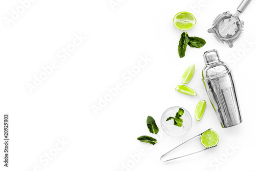 Process of making mojito concept. Ingredients and crockery. Slices of lime, mint, glass with ice cubes, shaker, strainer on white background top view copy space