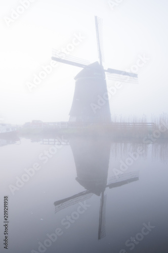 Windmill and reflection in fog at dawn, Netherlands.