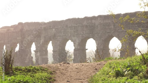 Stunning view of roman aqueduct claudio ruins arches in parco degli acquedotti park ruins in rome on romantic misty sunrise landscape with hill dirt road and trees photo