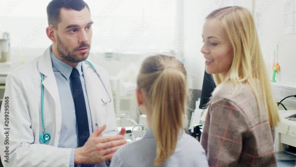 Friendly Doctor Does Routine Examination of a Sweet Little Girl who Came with Her Mother. Pediatrician Talks to Both of them. Doctor's Office is Bright and Modern. Friendly Doctor Does Routine Examination of a Sweet Little Girl who Came with Her Mother. Pediatrician Talks to Both of them. Doctor's Office is Bright and Modern.