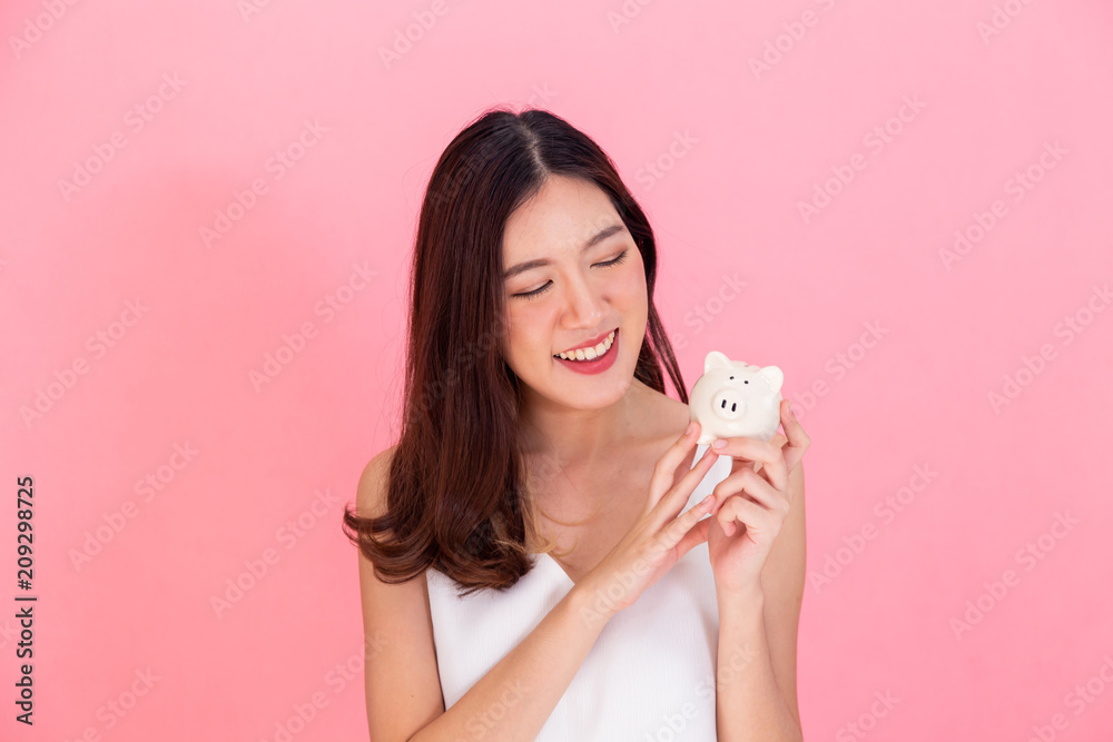 Portrait of young Asian woman holding a piggy bank, happy and excited over own saving isolated over vivid pink background Portrait of young Asian woman holding a piggy bank, happy and excited over own saving isolated over vivid pink background