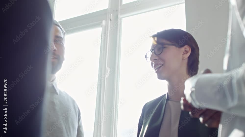 Cheerful mid-aged businessman standing by the window in office, smiling and talking with young multiethnic colleagues Cheerful mid-aged businessman standing by the window in office, smiling and talking with young multiethnic colleagues