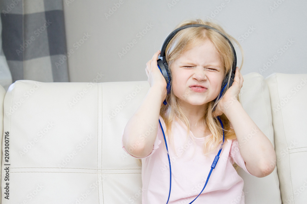 Music, gadget, childhood concept - cheerful blonde little girl in headphones listening to music and sitting at home Music, gadget, childhood concept - cheerful blonde little girl in headphones listening to music and sitting at home