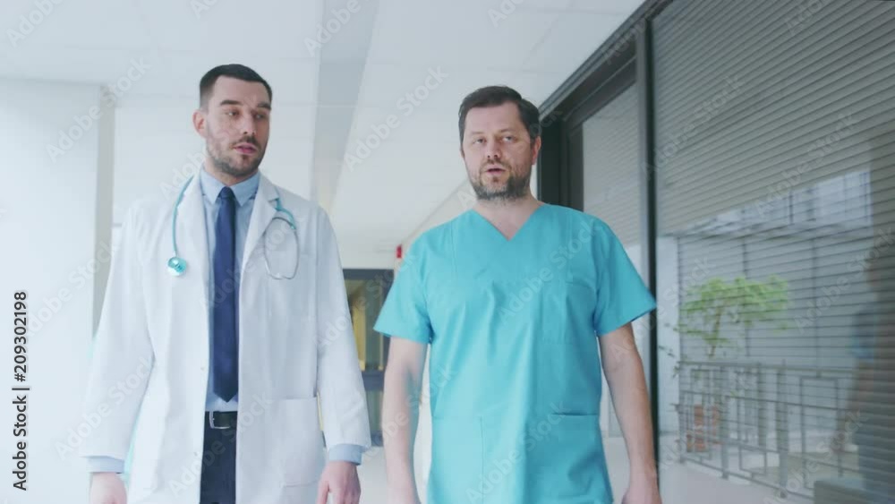 Surgeon and Doctor Talking, Walk Through Hospital Hallway in a Hurry. Modern Bright Hospital with Professional Staff. Shot on RED EPIC-W 8K Helium Cinema Camera. Surgeon and Doctor Talking, Walk Through Hospital Hallway in a Hurry. Modern Bright Hospital with Professional Staff. Shot on RED EPIC-W 8K Helium Cinema Camera.