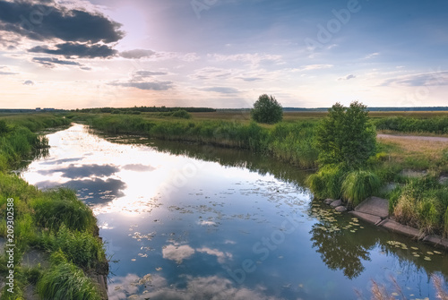 Landscape before sunset with a river and grass in the field