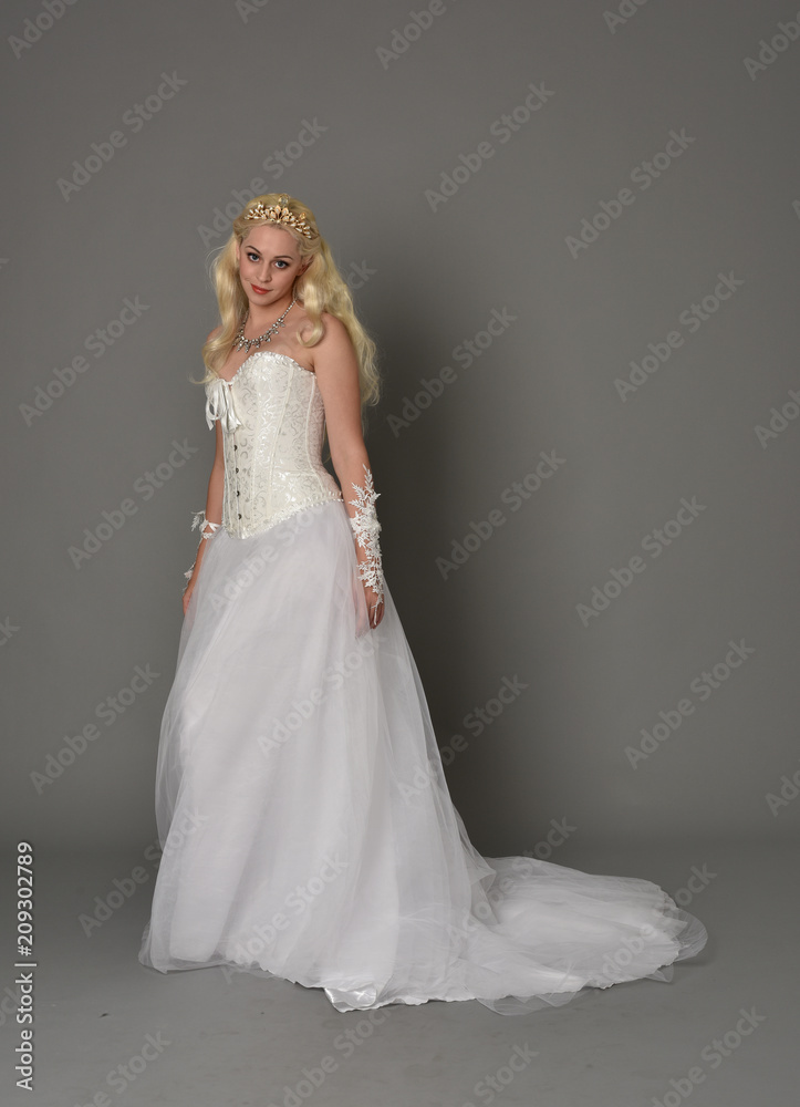 full length portrait of blonde girl wearing white corset gown. standing pose on grey studio background.