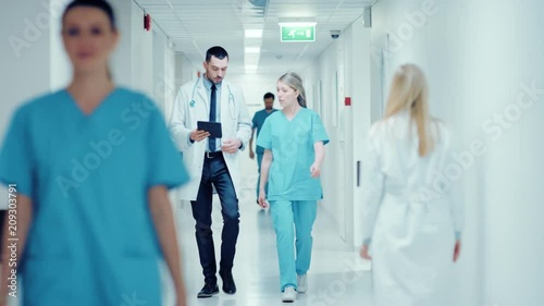 Surgeon and Female Doctor Walk Through Hospital Hallway, They Consult Digital Tablet Computer while Talking about Patient's Health. Shot on RED EPIC-W 8K Helium Cinema Camera. photo
